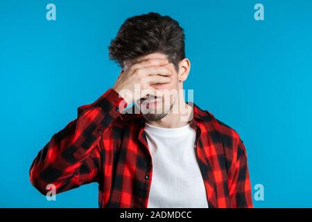 Jungen Kerl bedeckt sein Gesicht mit den Händen von tödlichen Enttäuschung, scheitern. Betätigt man in Red Plaid Shirt verloren. Dramatik, Emotionen Konzept. Stockfoto