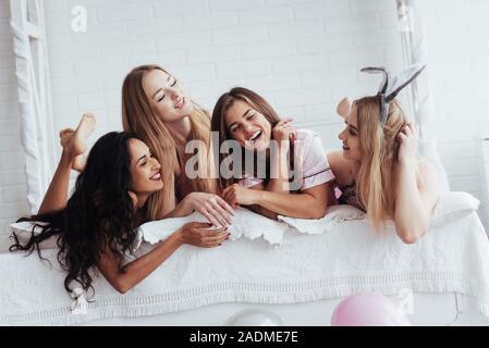 Ferien Zeit. Fröhliches Mädchen in der Nachtwäsche auf dem Bett liegend in weißen Raum und haben Feier Stockfoto