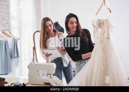 Zwei Mädchen haben gute Kleid maked. Der Prozess der Montage das Kleid im Studio von Hand gestaltete Kleidung Stockfoto