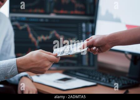 Prozess von Geben und Empfangen von Geld. Tag der Gehalt im modernen Büro mit Bildschirmen mit Grafiken auf ihnen Stockfoto