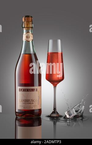 Flasche Sekt Lamrusco rosato mit Weinglas auf dem grauen Hintergrund. Spritzer Eiswürfel. Stockfoto