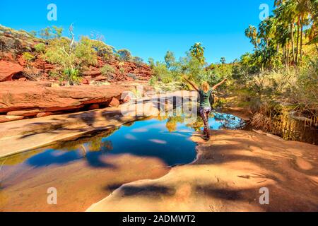 Frau sorglos genießen Sandsteinfelsen und Rotkohl Palm am Wasserloch im Palm Valley Oasis, Finke Gorge National Park wider. Tourismus Outback Stockfoto