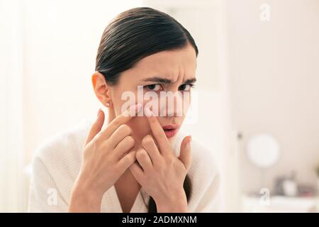 Ernsthafte Frau quetschen Pickel im Gesicht und runzelte die Stirn Stockfoto