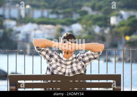 Rückansicht Porträt eines Mannes entspannten sitzen auf einer Bank, die in einem Ozean Küste Stadt Stockfoto