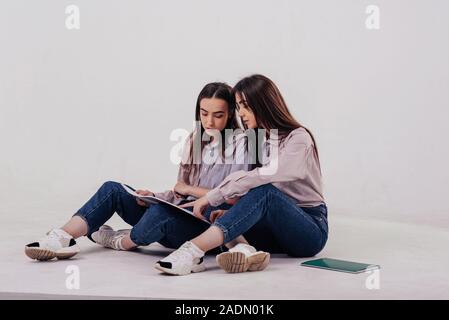 Die jungen Schüler und Schülerinnen lernen, neue Sachen. Zwei Schwestern, die Zwillinge sitzen und im Studio posiert mit weißem Hintergrund Stockfoto