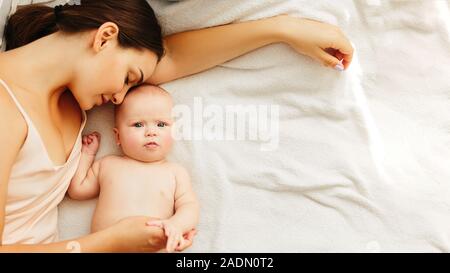 Junge schöne Mutter liegt mit dem Baby auf dem Bett, sanft Küsse, zusammen schlafen. Stockfoto