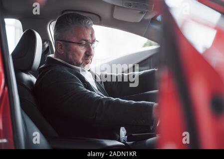 Versuchen, neue Funktionen. Seitenansicht der älteren Geschäftsmann in der offiziellen Kleidung fahren ein modernes neues Auto Stockfoto