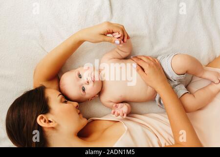 Junge schöne Mutter liegt mit dem Baby auf dem Bett, sanft Küsse, zusammen schlafen. Stockfoto