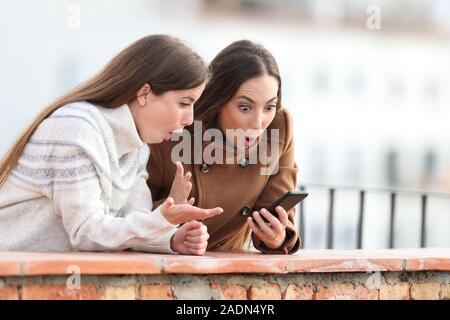 Überrascht Frauen handy news im Winter auf einem Balkon in einer ländlichen Stadt Stockfoto