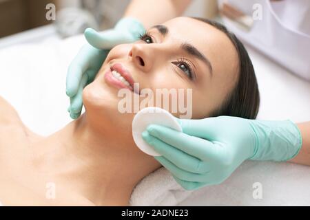Sorgfältige cosmetologist Reinigung der Haut von Gesicht von Happy lady Stockfoto