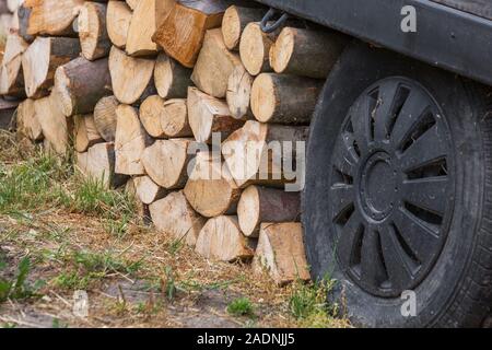 Stapel von Brennholz liegt auf dem grünen Rasen auf der Straße, neben dem es unterstützt ein Rad mit einer Metallscheibe und einem Gummireifen Stockfoto