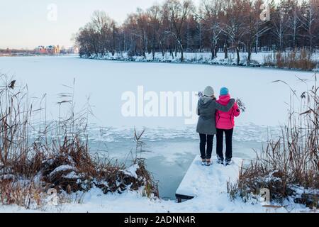 Winter gehen. Mutter und erwachsene Tochter bewundern verschneiten See Landschaft. Familie umarmen, erholsamer Urlaub Stockfoto