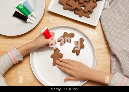 Die Hände des Kindes Dekorieren ein Weihnachten Lebkuchen cookies mit farbigen glazeon, Holz- Tabelle, Ansicht von oben. Weihnachtsplätzchen. Stockfoto