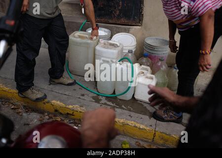 Caracas, Miranda, Venezuela. 29 Nov, 2019. Aura, ihr Mann und Sohn befüllen das Wasser contaners mit dem Wasser aus der Aura's Schwester Haus. Aura Graciela Sarmiento, Alter 56, und ihr Mann Jose Alberto Abreu, Alter 62, habe keine fliessendes Wasser in Ihrem Haus in 4 Jahren. Aura arbeitet in ein Geschäft mit Büromöbeln und Jose ist ein Mechaniker. Sie leben in der Nähe von Altos de Lidice in Caracas Venezuela. Altos de Lidice ist ein historisches Chavista Nachbarschaft. Aber Aura ist pro-Opposition, und hat nie die Chavez Regime unterstützt, obwohl sie in diesem pro lebten - Chavez/Maduro Stockfoto