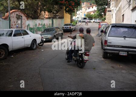 Caracas, Miranda, Venezuela. 29 Nov, 2019. Den Ehemann von Aura und Sohn fahren mit vollen Behältern nach Hause zu bringen, während die Aura hält die andere. Aura Graciela Sarmiento, Alter 56, und ihr Mann Jose Alberto Abreu, Alter 62, habe keine fliessendes Wasser in Ihrem Haus in 4 Jahren. Aura arbeitet in ein Geschäft mit Büromöbeln und Jose ist ein Mechaniker. Sie leben in der Nähe von Altos de Lidice in Caracas Venezuela. Altos de Lidice ist ein historisches Chavista Nachbarschaft. Aber Aura ist pro-Opposition, und hat nie die Chavez Regime unterstützt, obwohl sie in diesem pro lebten - chavín Stockfoto