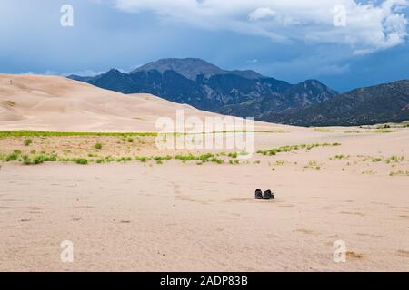 Ein paar Stiefel auf den Dünen links unterhalb der Rocky Mountains und einem stürmischen Himmel verlassen Stockfoto