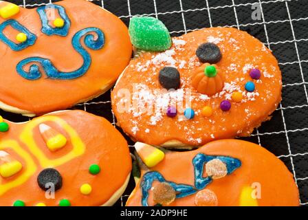 Halloween Kürbis geformte Sugar Cookies in hellen orange Puderzucker bedeckt und abgerundet mit verschiedenen Süßigkeiten. Stockfoto