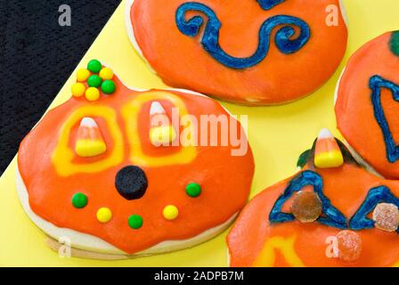 Halloween Kürbis geformte Sugar Cookies in hellen orange Puderzucker bedeckt und abgerundet mit verschiedenen Süßigkeiten. Stockfoto