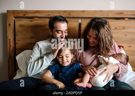 Glücklich liebende Familie gekuschelt auf dem Bett mit Neugeborenen und 4 Jahre alt Stockfoto