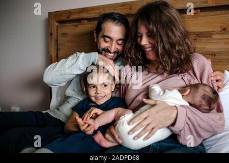 Lächelnd Familie zusammen auf dem Bett kuschelte als Mutter stillen Neugeborenes Stockfoto