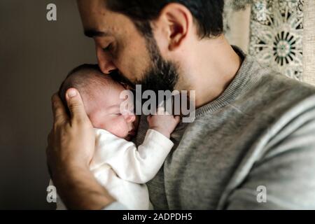 Bärtige Vater küsst liebevoll Leiter der Neugeborene schlafen in seine Arme Stockfoto