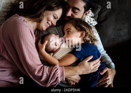 Vater umarmt Familie als Mutter lächelt bei 4 Jahre alten und Neugeborenen. Stockfoto