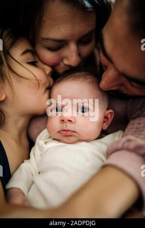 Papa, Mama und große Schwester küssen neugeborenes Baby Stockfoto