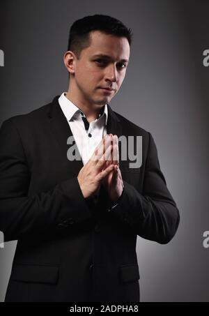 Ernsthafte denken Mann, der betet und Suchen im schwarzen Anzug in Grau studio Hintergrund. Closeup Portrait. Stockfoto