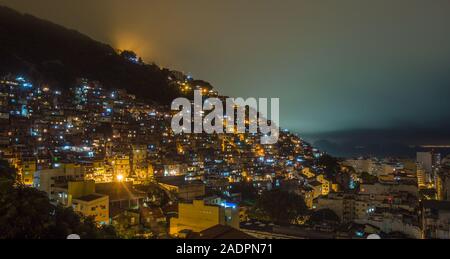 Nacht über das brasilianische Favelas auf dem Hügel mit City Downtown unten, Rio De Janeiro, Brasilien Stockfoto