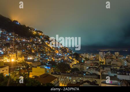 Nacht über das brasilianische Favelas auf dem Hügel mit City Downtown unten, Rio De Janeiro, Brasilien Stockfoto