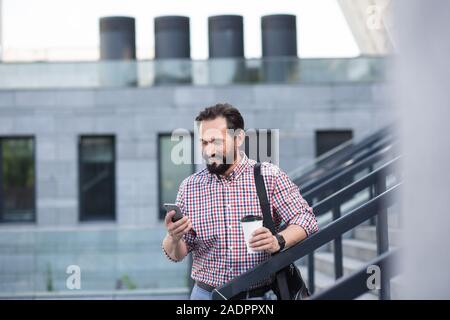 Positive stattlicher Mann mit Telefon, während Kaffee trinken Stockfoto