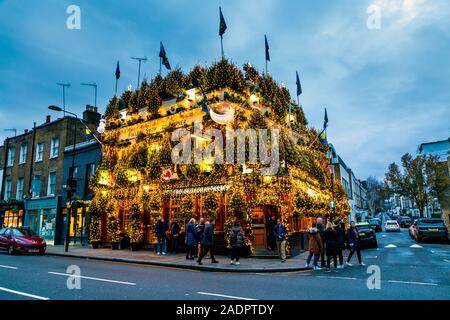Opulente Weihnachtslichter und Dekorationen an der Fassade des Churchill Arms Pub, London, Großbritannien Stockfoto