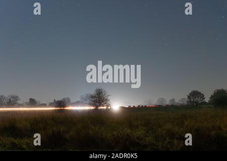 Verkehr Trails, über gemeinsame Land mit Kühen in der Ferne. Auf einem Winter Nacht in der Landschaft. Stockfoto