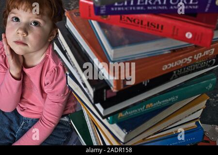 Volksschule Student von riesigen Stapel Lehrbücher, die sie braucht, um ihre Ausbildung zu vervollständigen Lesen eingeschüchtert Stockfoto