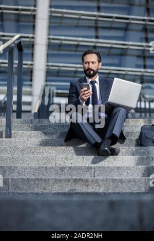 Ernsthafte Geschäftsmann mit seinem Laptop auf der Treppe Stockfoto