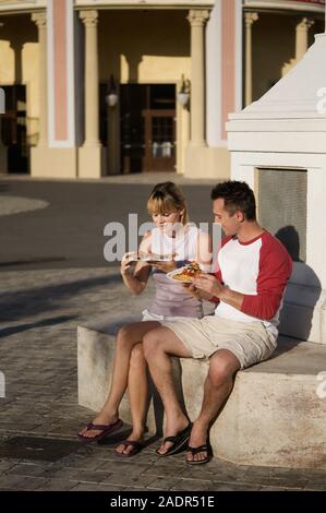 Junges Paar isst eine Pizzaschnitte - Junges Paar essen Pizza im Freien Stockfoto