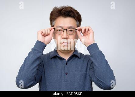 Asiatische Männer mittleren Alters, die versuchen, aus Gläsern zu nehmen und etwas sehen. schlechte Sicht, alterssichtigkeit, Kurzsichtigkeit. Stockfoto