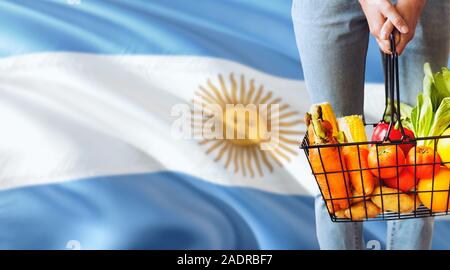 Frau hält Supermarkt Korb, Argentinien wehende Flagge Hintergrund. Wirtschaft Konzept für frisches Obst und Gemüse. Stockfoto