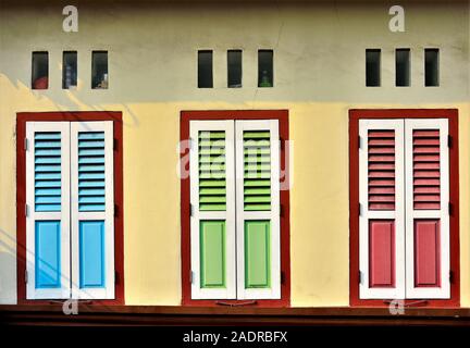 Nahaufnahme von Vintage windows mit antiken blauen, grünen und roten Fensterläden aus Holz auf der gelben Wand von shophouse im historischen Little India, Singapur Stockfoto