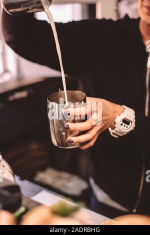 Zugeschnittenes Bild der weiblichen Barista gießen Milch von Krug zu Krug Stockfoto