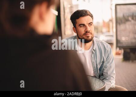 Nachdenklicher Mann sitzt mit seiner Freundin im Straßencafé Stockfoto