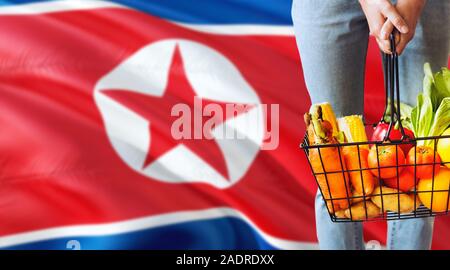 Frau hält Supermarkt Korb, Nordkorea wehende Flagge Hintergrund. Wirtschaft Konzept für frisches Obst und Gemüse. Stockfoto