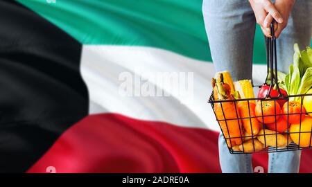 Frau hält Supermarkt Korb, Kuwait wehende Flagge Hintergrund. Wirtschaft Konzept für frisches Obst und Gemüse. Stockfoto