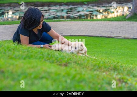 Asiatische Frau ihr goldenes Welpen knuddeln auf dem grünen Rasen Stockfoto