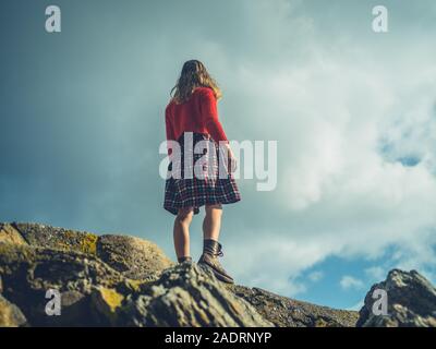 Eine junge Frau steht auf einem Felsen vor blauem Himmel Stockfoto