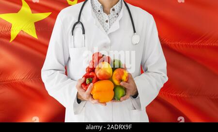 Arzt hält Obst und Gemüse in den Händen mit China Flagge Hintergrund. Nationalen Gesundheitswesen Konzept, medizinische Thema. Stockfoto