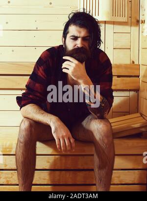 Mann traurig oder Badende, bärtigen Hipster mit Bart und Schnurrbart in rot kariertem Hemd nass von Wasser in der Sauna sitzt, Thermalbad auf hölzernen Hintergrund Stockfoto