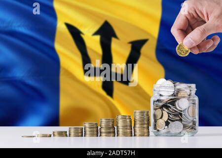 Business Mann mit Münzen, Glas, Barbados Flagge schwenkten im Hintergrund. Finanzen und Business Konzept. Spart Geld. Stockfoto