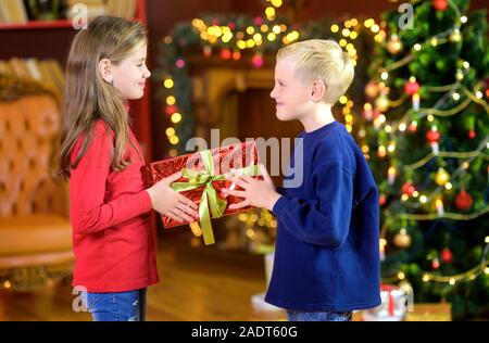 Kinder Geschenke beim Stehen in einem Zimmer auf dem Hintergrund einer Festliche Baum. Weihnachten und neues Jahr Stockfoto