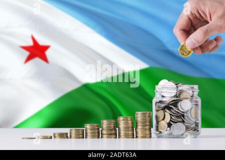 Business Mann mit Münzen, Glas, Dschibuti Flagge schwenkten im Hintergrund. Finanzen und Business Konzept. Spart Geld. Stockfoto